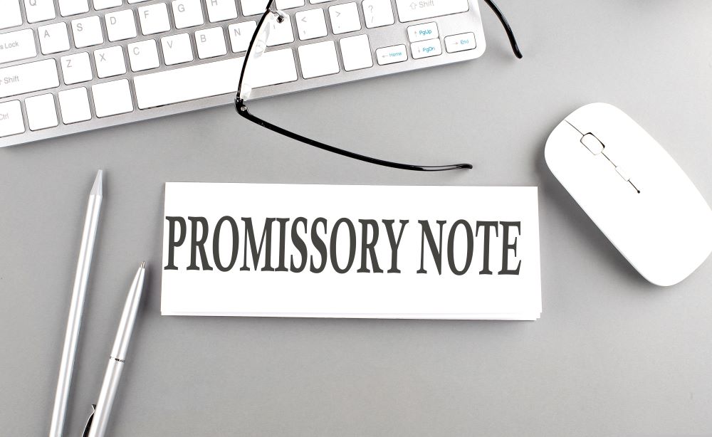 A worker has a piece of paper reading, 'Promissory Note' beside his computer, indicating that he intends on using funds from his Self-Directed IRA to provide someone else with a loan.