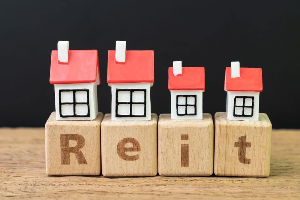 Blocks that spell out "REIT" with miniature houses on top of each block.