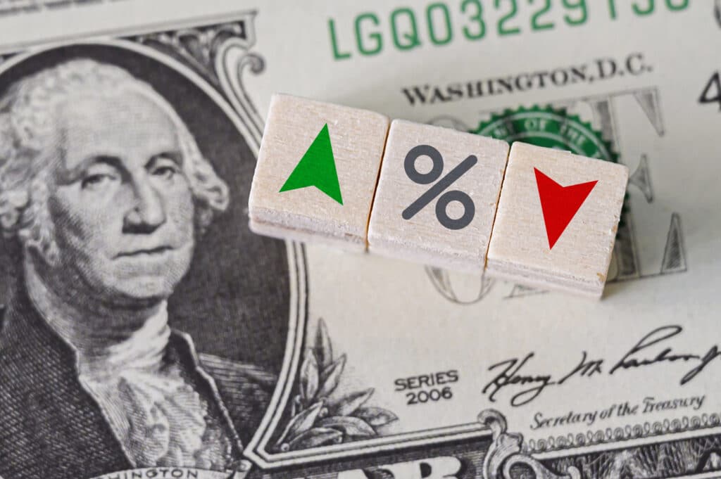 U.S. Dollar background with percentage icon and arrow symbols on wooden cube indicating interest rate increase and decrease by the Federal Reserve.
