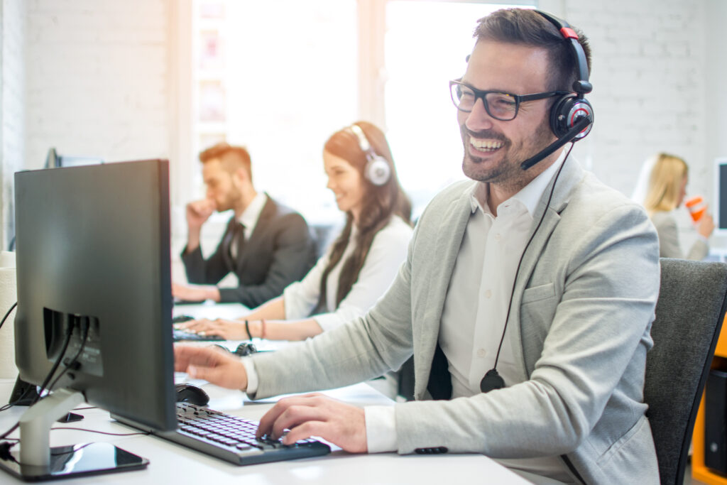 Friendly and knowledgeable customer support specialists in a call center with a headsets on and looking at computers.