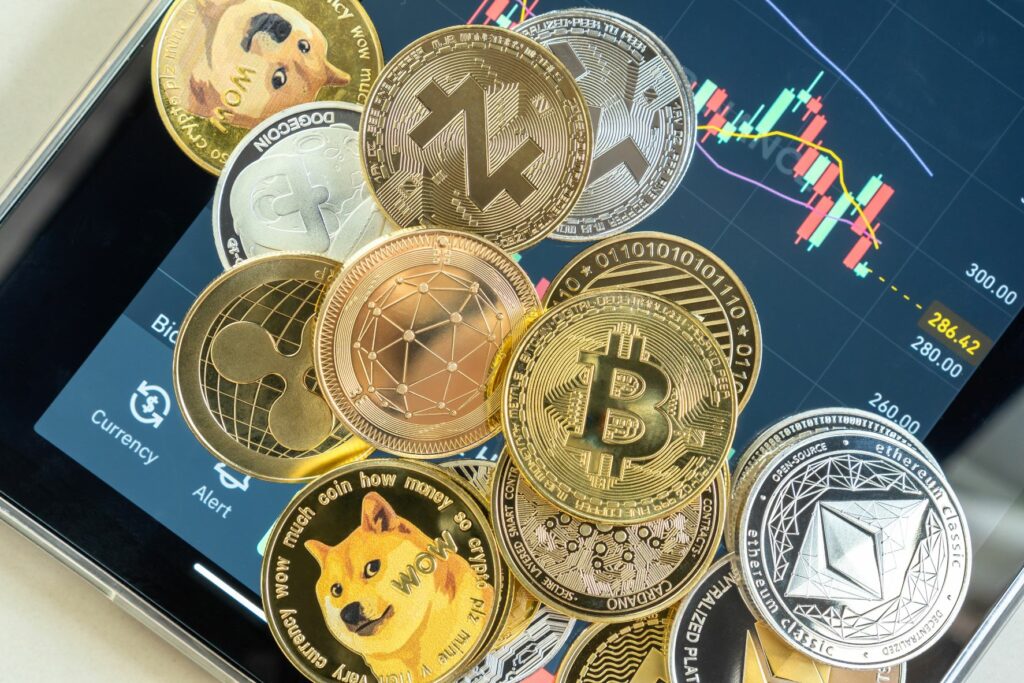 Pile of cryptocurrencies, including Bitcoin, Ethereum, Litecoin, and Dogecoin on top of a tablet with a fluctuating graph on the Binance trading app in the background. 
