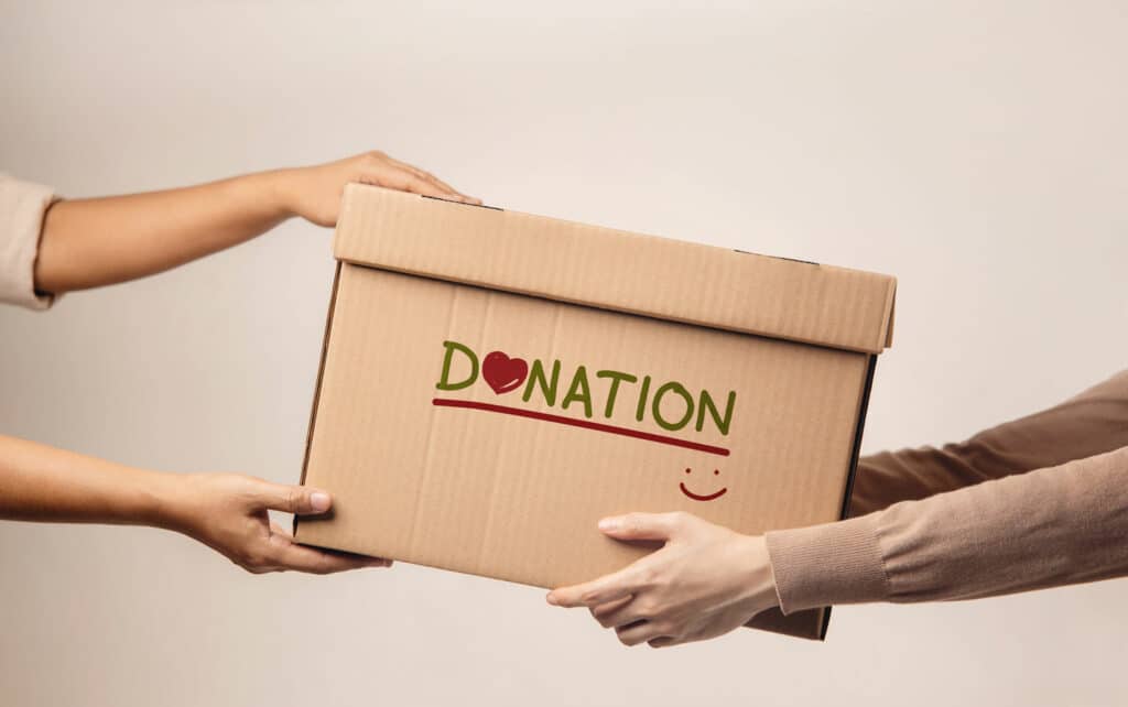 One person handing a box that says “donation” with a smiley face on it to another person, signifying a qualified charitable donation from their IRA.