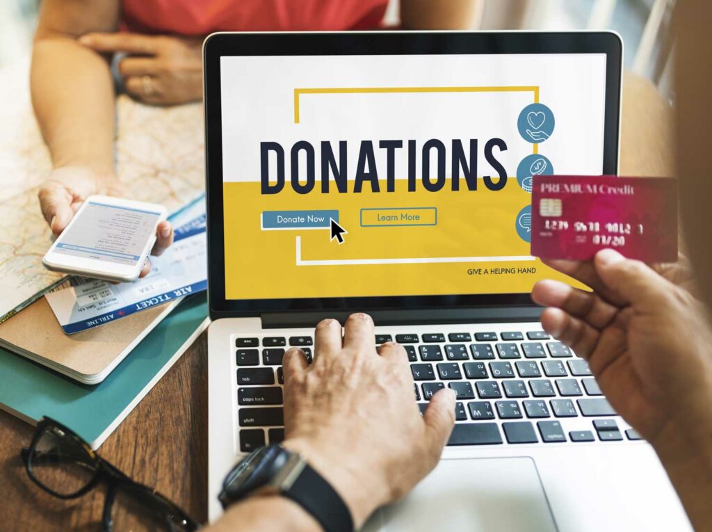 A tax-deferred IRA account holder making a qualified charitable distribution on their laptop that says “Donations” and holding a red credit card.