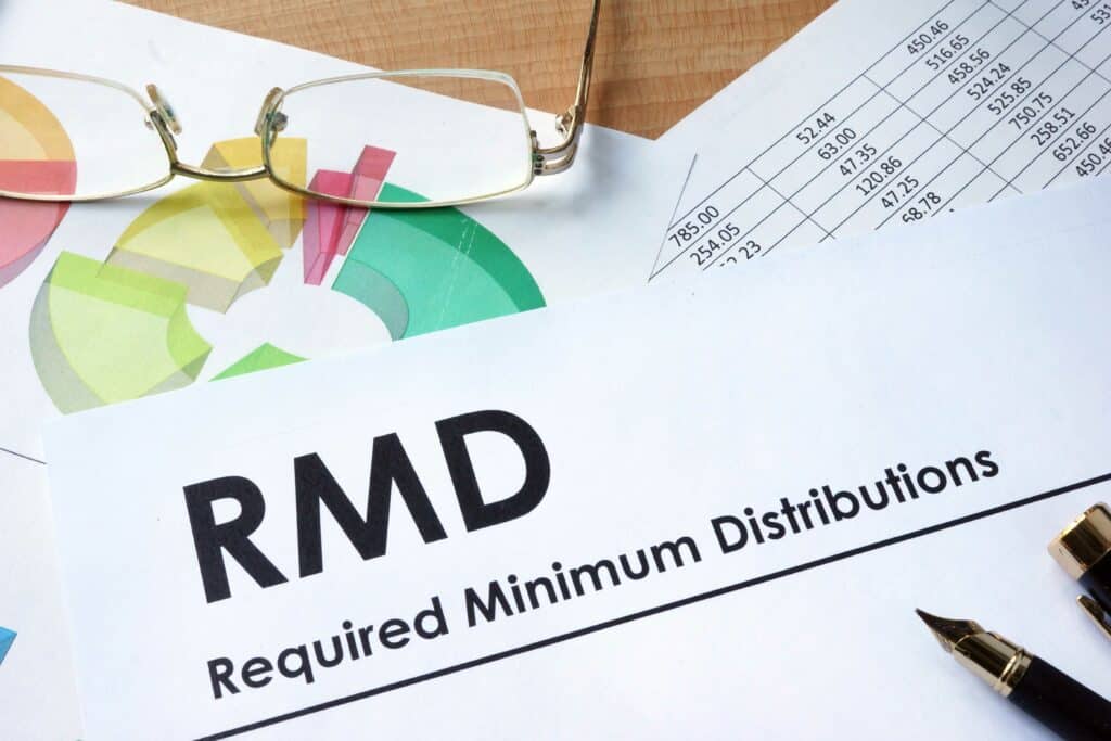 Paper that says “RMD: Required Minimum Distributions” on it next to graphs and glasses, to display that a qualified charitable distribution can satisfy an IRA account holder’s RMD. 