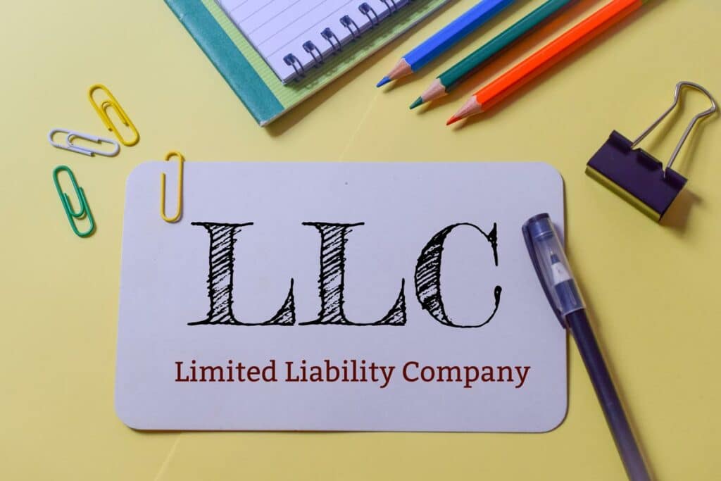 Purple notecard that says “LLC - Limited Liability Company” on a table with notebook, pencils, and paperclips next to it.
