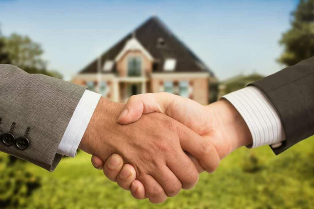 Two businessmen shaking hands in front of a real estate investment property to display the deal between the non-recourse lender and the borrower.