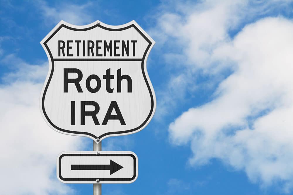 Street sign that says “Retirement: Roth IRA” with arrow pointing right and blue sky and clouds in the background.
