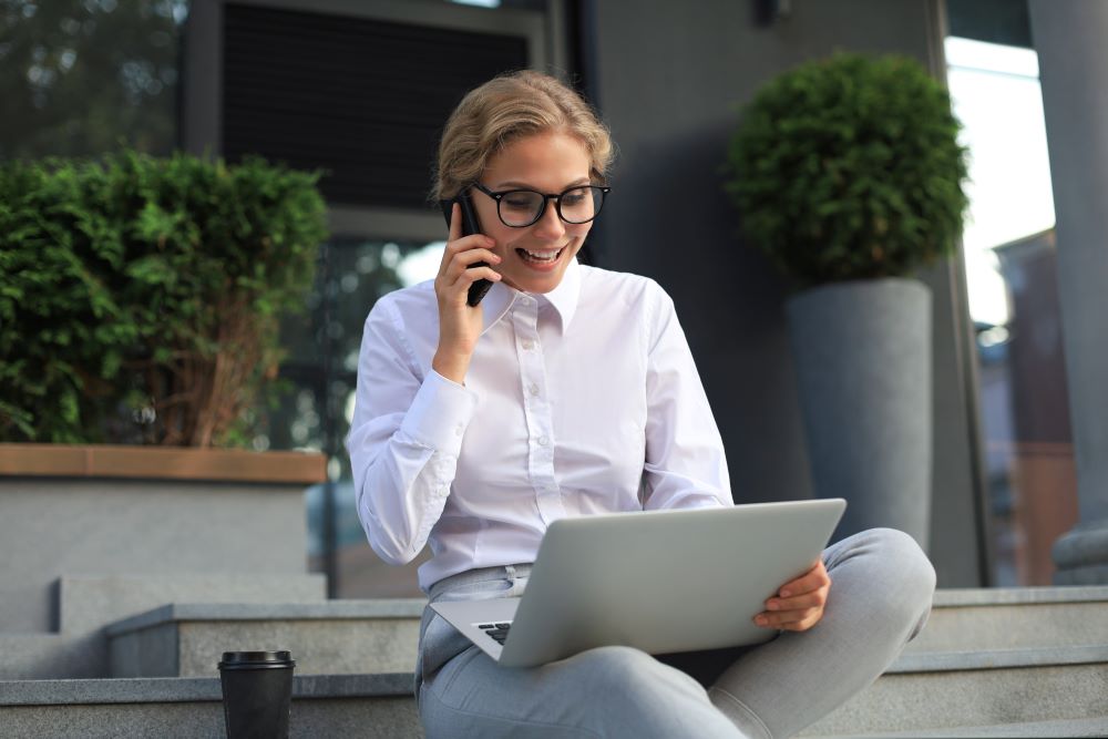 Happy entrepreneur working with a phone and laptop to explore the Benefits of a Self-Directed Solo 401(k) for Self-Employed Individuals