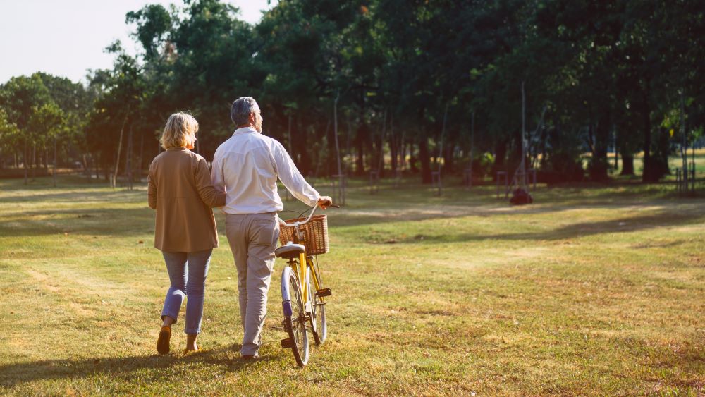 A relaxed couple pushes a bike across a field as they enjoy the leisurely days of retirement.
