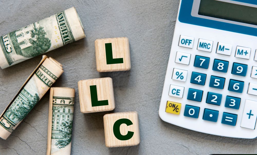 LLC ( - Limited Liability Company) acronym on wooden cubes on a gray background with a calculator and banknotes